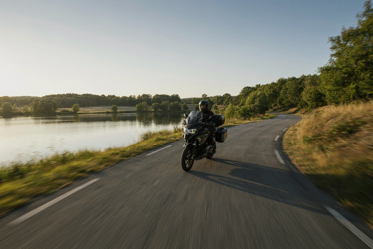 Moto évoluant sur une route sinueuse au bord du lac de Madine, au couchant